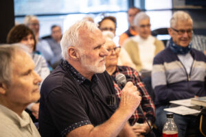 En som stiller spørsmål i mikrofonen, med mange mennesker rundt seg