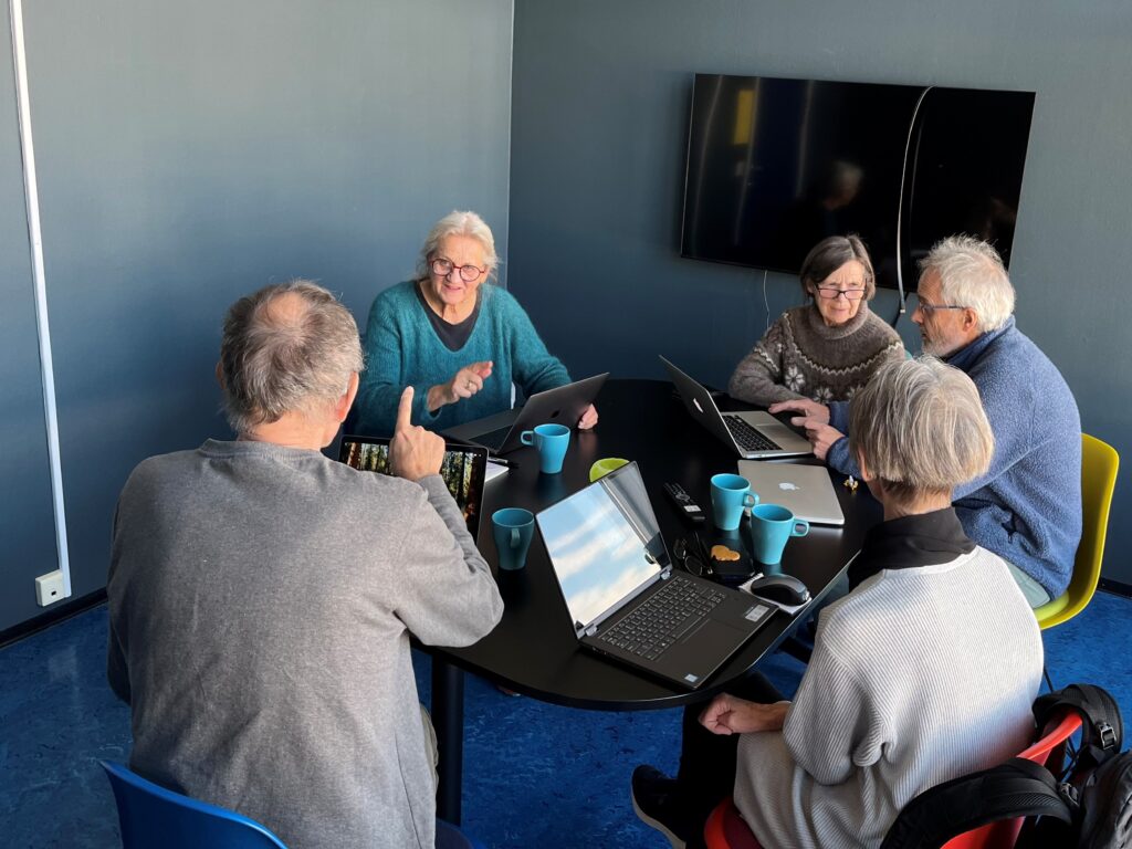Fem menneskser sitter ved et rundt bord og snakker sammen